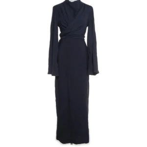 Marinblå omlottklänning med rosett - Snygg marinblå långklänning med omlott-design och v-ringad hals. Klänningen har långa ärmar och ett knytband i midjan som ger en fin rosett baktill. Materialet ser ut att vara mjukt och följsamt, perfekt för dig som gillar stilrena och eleganta plagg.