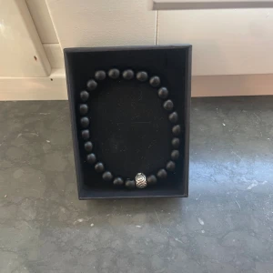 Svart pärlarmband med silverdetalj - Stilrent svart armband med runda pärlor och en snygg silverfärgad detalj med mönster. Perfekt accessoar för dig som gillar minimalistisk design och vill ha något som sticker ut lite extra. Kommer i en elegant svart ask.