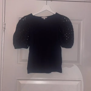 Marinblå blus med puffärmar från H&M - Är helt ny utan prislapp. Säljer en marinblå blus från H&M med puffiga kortärmar i broderad spets och rund halsring.