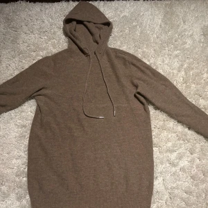 Kaschmir hoodie - Mysig beige kaschmir hoodie med huva och dragsko. Tröjan har lång ärm och ribbade muddar vid ärmslut och nederkant. Perfekt för lager-på-lager och chill dagar. Den har litet mindre fel på framsidan vid bröst korgen inget som man märker.