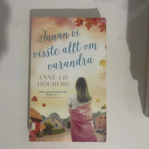 Innan vi visste allt om varandra - En gripande och fantastisk roman om relationer och livet, perfekt för dig som gillar känslomässiga berättelser. Omslaget visar en person insvept i en filt, med höstlöv och hus i bakgrunden, vilket ger en varm och inbjudande känsla.