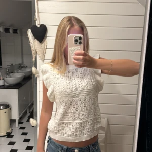 Vit stickad blus med volangärmar - Supersöt vit stickad blus med volangdetaljer vid ärmar och hals. Mönstrad med olika stickade strukturer och hålmönster som ger en romantisk vibe. Croppad passform och ribbade kanter. Perfekt att styla med jeans eller en lång kjol❣️❣️