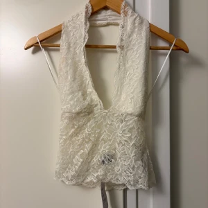 Vit spetsig omlott-linnetopp - Supersnygg vit linne-topp i spets med djup v-ringning och omlottkänsla. Blommigt spetsmönster, croppad passform och tunna axelband. Perfekt för dig som vill sticka ut med en feminin och trendig look. Aldrig använd och har prislappen kvar