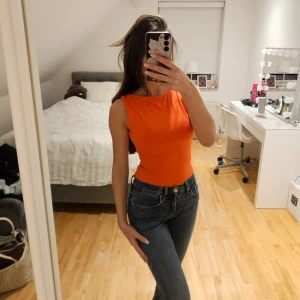 Orange ärmlös topp med öppen rygg - Säljer en snygg röd ärmlös topp med rund halsringning och en riktigt öppen rygg. Toppen är figurnära och har en enkel, stilren design som sticker ut med sin starka färg. Perfekt för dig som vill ha något färgstarkt och trendigt.