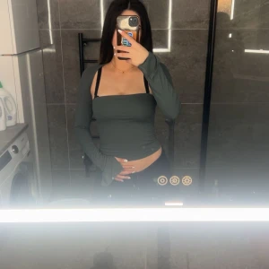 Mörkgrön långärmad tubtopp - Säljer en mörkgrön, tight och croppad tubtopp med långa ärmar. Toppen har en stilren, axelbandslös design och sitter snyggt figurnära. Perfekt för dig som gillar minimalistisk stil med en twist.