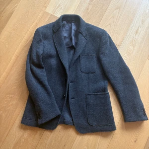 Grå kavaj från Dondup i ull - Snygg grå kavaj från Dondup, tillverkad i mjuk ull med slät grått foder. Klassisk design med tre framfickor, tre knappar vid ärmslut och markerade sömmar. Köpt för 4500kr säljer för 999kr