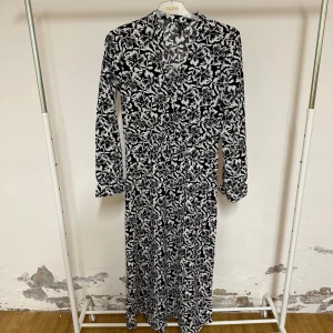 Svartvit blommig långklänning Vero Moda - Snygg långklänning från Vero Moda med svartvit blommigt mönster. Klänningen har v-ringad hals, långa ärmar och är tillverkad i ett mjukt material som känns skönt mot huden. Perfekt för dig som gillar stilrena och trendiga prints.