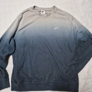 Nike sweatshirt i grått och blått - Nike sweatshirt med snygg ombre-effekt från ljusgrå upptill till mörkblå nedtill. Klassisk rund halsringning och långärmad modell. Liten Nike-logga broderad på bröstet. Perfekt för en chill och sportig stil.