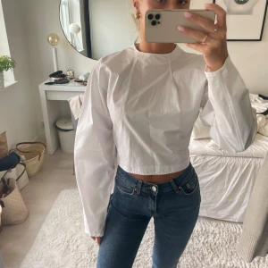 Vit blus med öppen rygg - Säljer en vit croppad blus i bomull med långa ärmar och rund hals. Baksidan har en stor öppen rygg med knäppning i nacken och knytband i midjan. Perfekt för dig som gillar stilrena och unika detaljer. Från zara aldrig använd 