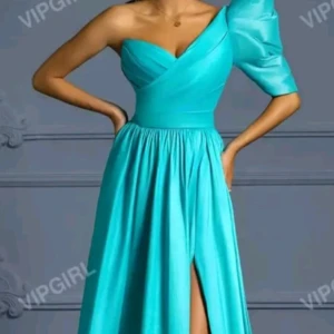 Turkos långklänning med snörning - Snygg turkos långklänning med en axel och puffärm. Klänningen har en markerad midja, slits framtill och v-ringad överdel. Baksidan har  snörningsdetalj som gör att size XS, S och eventuellt M kan passa. Perfekt för dig som vill sticka ut med en unik och trendig look. Perfekt för balklänning 😍