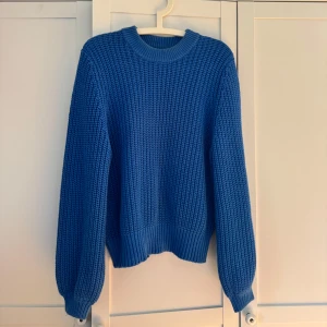 Blå stickad tröja med grov struktur - Säljer en blå stickad tröja med grov struktur och rund halsringning. Tröjan har långa ärmar och breda muddar vid ärmslut och nederkant. 