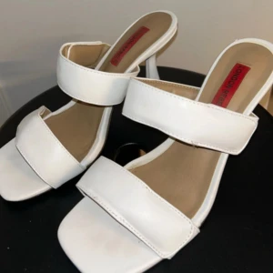 Vita klackar från London Rebel - Snygga vita klackar från London Rebel med två breda remmar och fyrkantig tå. Skorna har en smal hög klack och öppen häl, vilket ger en trendig och stilren look. Tillverkade i syntetmaterial med ljus innersula. Skorna är knappt använda och därav i topp skick. True to size. Ny pris: 499kr