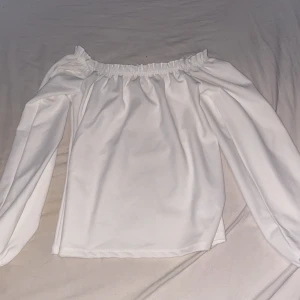 Vit offshoulder topp med långa ärmar - Snygg vit offshoulder topp med långa ärmar och elastisk kant upptill som ger en trendig look. Perfekt för dig som gillar stilrena och enkla plagg. Toppens material känns mjukt och följsamt mot huden.