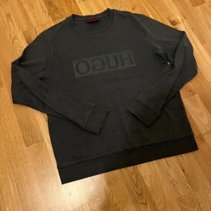 Vintage tröja från hugo boss - Snygg mörkgrå sweatshirt från Hugo boss med stort logotryck på bröstet. Storlek 170 men passar som S.