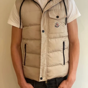 Moncler dunväst  - Säljer en beige dunväst från Moncler med huva. S men stor i storleken! Modellen är 187 och ca 70 kg. Passar perfekt till hösten 🍂! Skriv om du har några funderingar ✨( pris kan diskuteras)