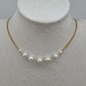 Guldfärgat halsband med pärlor - Stilrent halsband med guldfärgad kedja och sju vita pärlor i olika storlekar framtill. Kedjan har klassisk länkdesign och pärlorna ger en elegant touch. Perfekt accessoar för att lyfta din outfit.