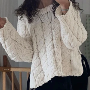 Vit stickad kabeltröja med breda ärmar - Supermysig vit stickad tröja med grovt kabelstickat mönster och breda, långa ärmar. Tröjan har en rund halsringning och en lite loose passform som ger en chill vibe. Perfekt att slänga på sig när det är kallt ute.