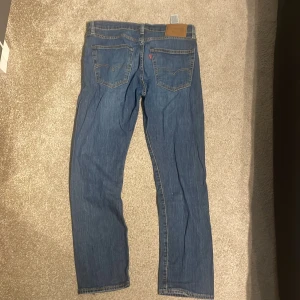 Levi's 502 blå jeans - Säljer ett par klassiska Levi's 511 jeans i blå denim. Modellen har en smal passform med raka ben och fem fickor. Typisk Levi's-detalj med röd etikett på bakfickan och läderpatch i midjan. Perfekta för dig som gillar en tidlös och clean look. Storlek 31/30
