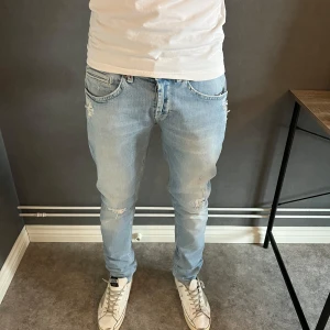 Ljusblå Dondup jeans med slitningar W32 - Säljer ett par ljusblå Dondup jeans med snygga slitningar och detaljer på både fram- och baksida. Jeansen har klassisk femficksdesign, dragkedjegylf och smal passform. Perfekta för dig som gillar en avslappnad men trendig look. Kom PM vid frågor!