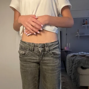 Grå lågmidjade jeans med raka ben - Säljer ett par grå jeans med låg midja och raka ben. Jeansen har dubbla knappar i midjan, klassiska fickor fram och bak samt en cool tvättad look. Perfekta för dig som gillar en avslappnad och trendig stil.