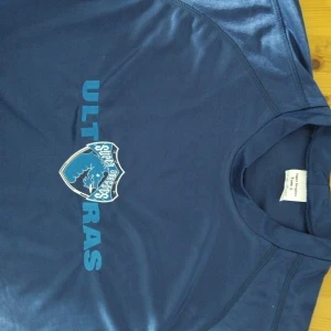 Blå fotbollströja Surf Orders Ultras Porto  - Porto Portugal ultrs super dragoes Snygg blå fotbollströja från Surf Orders med tryckt klubbmärke och texten 'ULTRAS' på bröstet. Tröjan är kortärmad och tillverkad i ett lätt, sportigt material som andas. Perfekt för dig som vill sticka ut på läktaren eller planen.