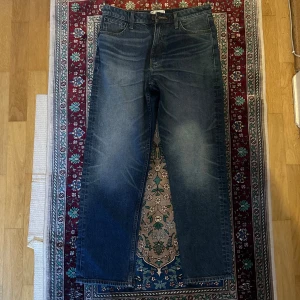 Blå raka jeans med klassisk tvätt - Säljer ett par blå jeans med klassisk tvätt och raka ben. Jeansen har fem fickor, bälteshällor och dragkedjegylf. Perfekta för dig som gillar en tidlös look och vill ha ett par jeans som funkar till det mesta.