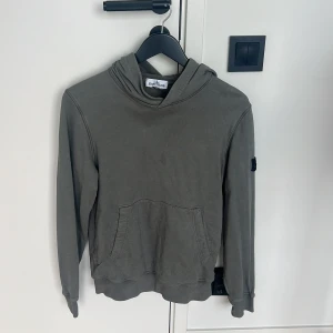 Grå hoodie från Stone Island Junior - Säljer en grå hoodie från Stone Island Junior med klassisk patch på ärmen. Den är i junior storlek 14 år men skulle säga den passar Xs/S/M i herrstorlek beroende på vikt. Hör av er vid frågor eller funderingar.