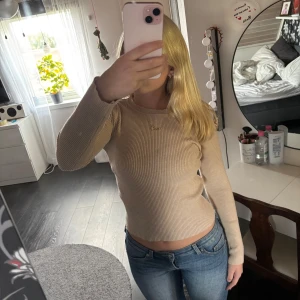 Beige ribbad långärmad tröja - Säljer en beige ribbad långärmad tröja med rund halsringning. Tröjan är figurnära och har en enkel, stilren design som passar perfekt till jeans. Materialet är mjukt och stretchigt för en bekväm passform.