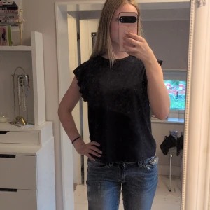 Marinblå volangtopp från Gina Tricot - Marinblå topp från Gina Tricot med volangdetaljer på axlarna. Modellen är ärmlös och har en rak passform. Tillverkad i mjuk bomull som känns skön mot huden. Perfekt flr dig som gillar en cute stil