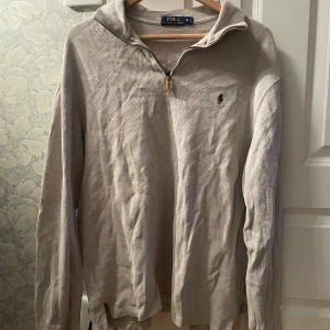 Beige half zip tröja Polo Ralph Lauren - Snygg beige långärmad tröja från Polo Ralph Lauren med half zip och klassisk krage. Tröjan har det ikoniska broderade logotypen på bröstet och är tillverkad i mjuk bomull. Perfekt för lager-på-lager och chill stil.