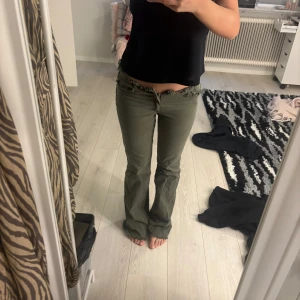 Olivgröna bootcut byxor med spets - Säljer ett par olivgröna byxor med bootcut passform och snygga spetsdetaljer i midjan och vid bensluten. Byxorna har låga midja och dragkedja framtill. Perfekta för dig som vill ha något unikt och trendigt i garderoben. Säljer då dem va för små