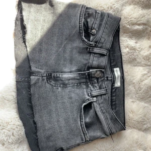 Lågmidjad grå jeanskjol - Säljer en grå, kort jeanskjol. Kjolen har klassiska jeansfickor fram och bak samt bälteshällor. 