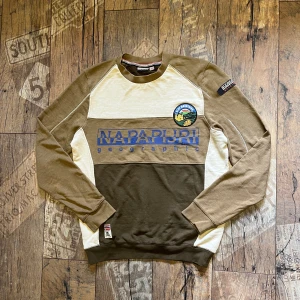 Beige och olivgrön tröja från Napapijri - Snygg långärmad tröja från Napapijri i beige och olivgrönt med stort tryck och patch på bröstet. Tröjan har rund halsringning, muddar vid ärmslut och midja samt coola kontrastpaneler. Perfekt för dig som gillar streetwear och outdoor vibes.