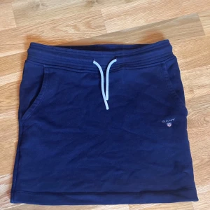 Mörkblå kortkjol från Gant - Mörkblå kortkjol från Gant med sportig känsla. Kjolen har snörning i midjan, fickor på sidorna och broderad Gant-logga framtill. Perfekt för en avslappnad och cool stil.