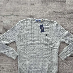 stickad tröja Polo Ralph Lauren - Kabelstickad grå tröja från Polo Ralph Lauren. Läng: 60 cm Axel bredd: 40 cm