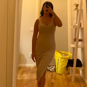 Beige ribbad midiklänning - Säljer en beige ribbad klänning med v-ringning och smala axelband. Klänningen är figurnära och har en asymmetrisk nederkant som ger en snygg siluett. Perfekt för dig som gillar enkel men stilren design.