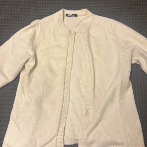Beige kofta från Gina Tricot - Mysig beige kofta från Gina Tricot med ribbade kanter och rund halsringning. Perfekt att slänga över en topp för extra värme. Enkel och stilren design som passar till det mesta.