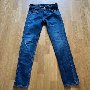 Replay Anbass slim jeans blå herr - Säljer ett par Replay Anbass slim fit jeans i klassisk blå tvätt med slitningar och snygga detaljer. Jeansen har fem fickor, dragkedjegylf och smal passform. Perfekta för dig som gillar en modern och stilren look. W30/L30