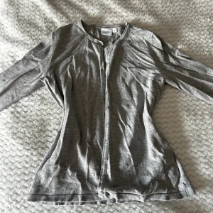 Grå kofta  - Säljer en stilren grå kofta från Saint i mjuk bomull. Koftan har rund halsringning, långa ärmar och knäppning framtill med små knappar. Perfekt att slänga över en t-shirt eller linne för en chill look. Kan sy in i midjan om det önskas för en mer figursydd look. Pris kan diskuteras! Hör av er vid frågor eller önskemål om fler bilder