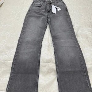 Grå raka jeans med hög midja - Snygga grå jeans med raka ben och hög midja. Klassisk femficksmodell i mjukt denimtyg, perfekt för en avslappnad och trendig look. Jeansen har dragkedjegylf och subtil tvätt för en modern känsla.