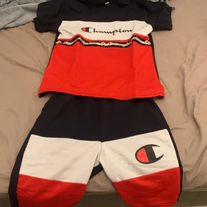 Champion shorts i rött, vitt och blått - Snygga Champion shorts i färgblock med rött, vitt och mörkblått. Stort Champion-logga på ena benet och elastisk midja för skön passform. Perfekta för chill eller sportiga dagar, matchar lätt med t-shirt eller hoodie.