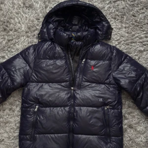 Mörkblå pufferjacka från Polo Ralph Lauren - Polo Ralph Lauren dunjacka – Mörkblå Storlek: S/XS Skick: Helt ny. Varm och lätt jacka med huva, perfekt för höst och vinter. Jag säljer jackan pågrund av den är för stor för mig. 