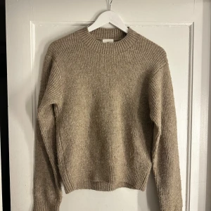 Beige stickad tröja från H&M - Mysig beige stickad tröja från H&M i storlek XS. Tröjan har ribbad struktur, rund halsringning och långa ärmar. Perfekt för lager-på-lager och chill höst- och vinterstil. Pris kan diskuteras 