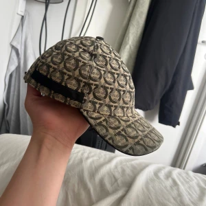 Beige och svart mönstrad keps - Snygg keps i beige och svart med ett grafiskt, återkommande mönster över hela ytan. Justerbar rem baktill och böjd skärm. Tillverkad i ett stadigt tyg som ger en cool och urban vibe. Perfekt accessoar för att lyfta din streetwear-look.