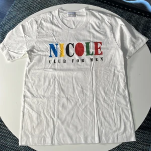 Vit t-shirt Nicole Club for Men - Vit t-shirt från Nicole Club for Men med färgglatt tryck på bröstet i blått, gult, svart, rött och grönt. Klassisk rund hals och korta ärmar. Tillverkad i mjuk bomull, perfekt för en clean och stilren look. Liten fläck, går nog bort i tvätt