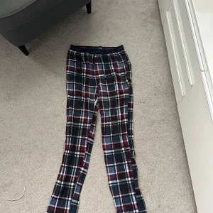 Rutig pyjamasbyxa från Jockey - Snygga rutig pyjamasbyxa från Jockey med elastisk midja och klassiskt rutmönster i mörkblått, vinrött och vitt. Byxorna är i mjukt bomullsmaterial och har en avslappnad passform, perfekta för chill dagar hemma.