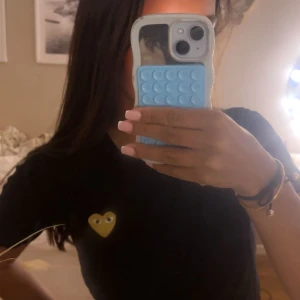 Svart Comme des Garçons t-shirt med hjärta - Svart t-shirt från Comme des Garçons Play med det ikoniska guldgula hjärtat med ögon broderat på bröstet. Klassisk passform och rund halsringning, perfekt för en clean och cool look. Storlek M men sitter som xs/s!!