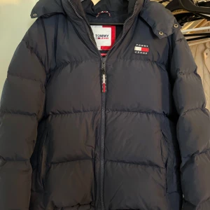 Tommy Hilfiger Pufferjacket - Säljer en mörkblå pufferjacka från Tommy Jeans, modell The Alaska Puffer. Jackan har huva, dragkedja framtill och broderad logga på bröstet. Perfekt för kalla dagar och riktigt snygg stil. Nypris 3000kr