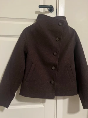 Mörkbrun kappa - Snygg mörkbrun kappa med hög krage och asymmetrisk knäppning framtill. 