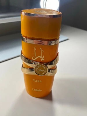 Yara parfym från Lattafa  - Snygg parfymflaska från Lattafa i modellen Yara. Flaskan är orange med gulddetaljer och har en unik, modern form. Märkets logga och namn syns tydligt på flaskan. Perfekt för dig som gillar trendiga och färgstarka accessoarer. 🧡